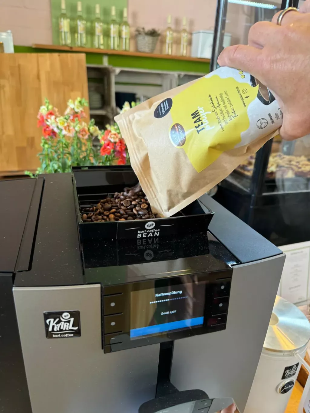 Eine Hand schüttet Kaffeebohnen von LiKe in eine Kaffeemaschine.