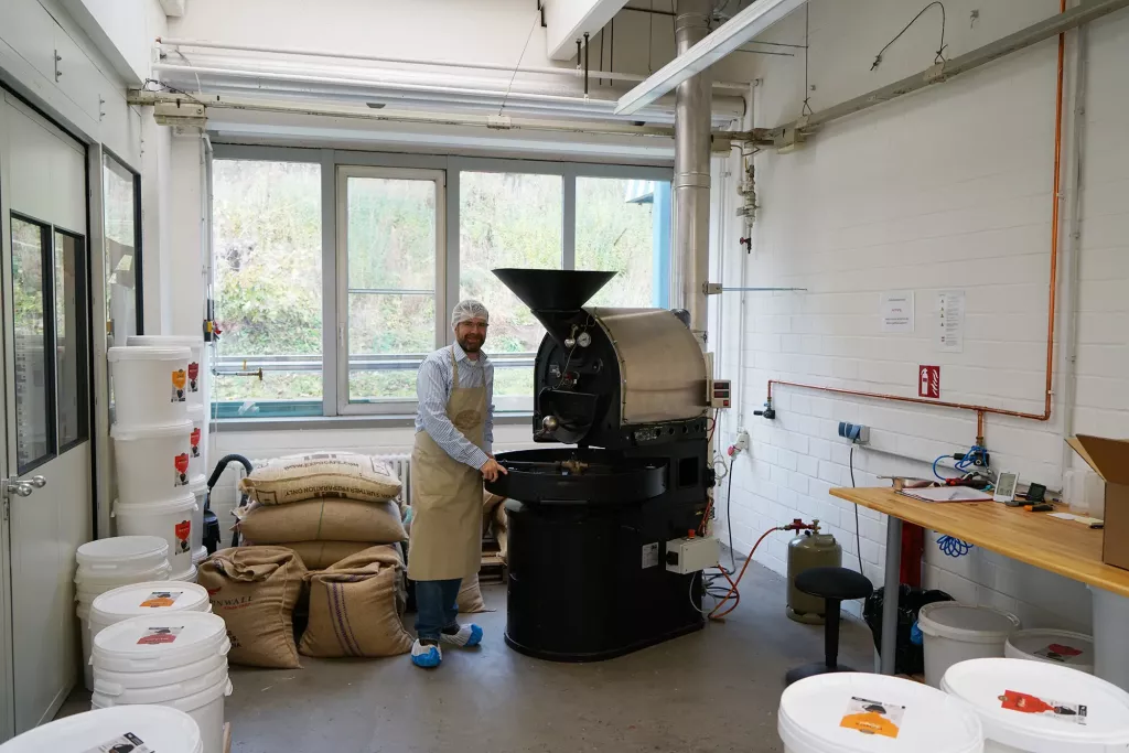 Markus Ratajczak steht neben seinem Trommelröster in seiner Kaffeerösterei.