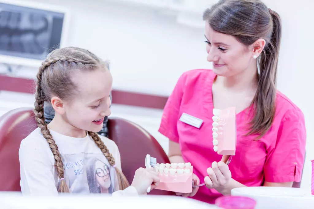 Ein Mädchen erhält eine Zahnputzschulung von einer Angestellten einer Zahnarztpraxis.