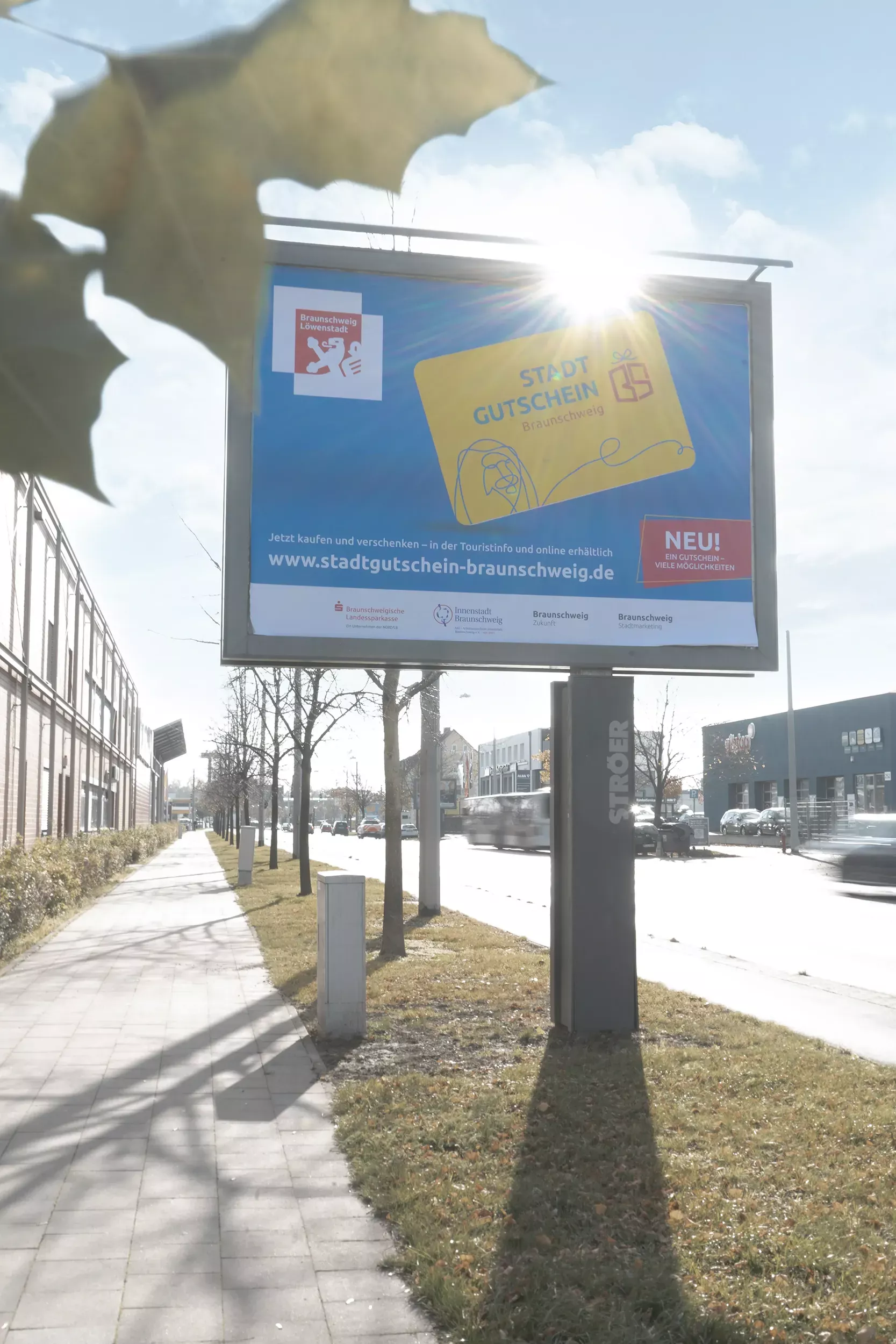 Eine Großfläche des Stadtgutscheins ist an einem Straßenrand zu sehen.