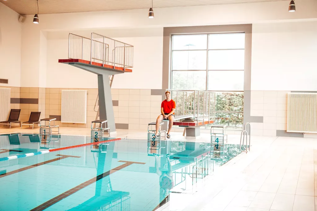 Ein junger Mann sitzt in einem Schwimmbad auf einem Sprungbrett.